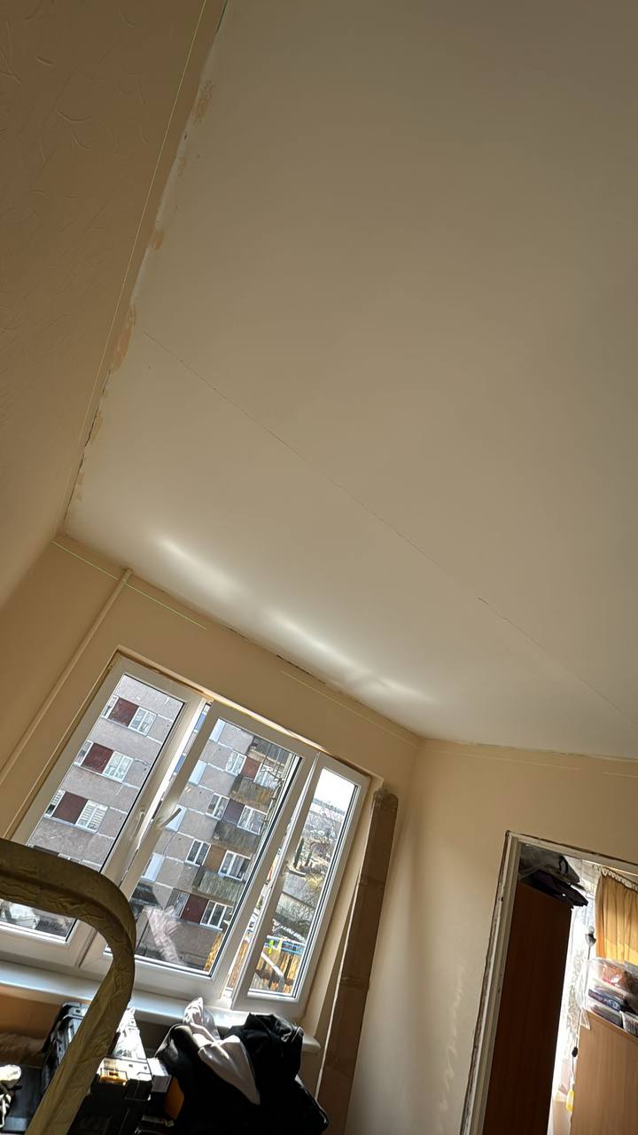 Matēti balti griesti ar stilīgu lustru viesistabā, kas piešķir eleganci un plašumu